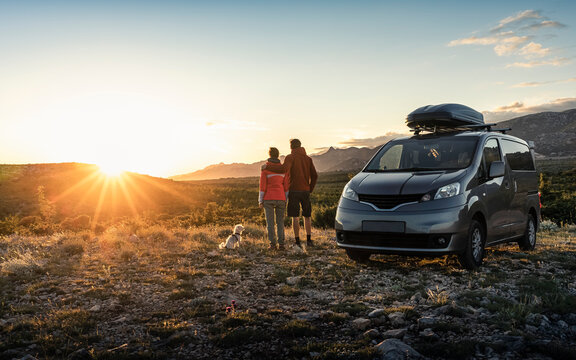 Man and woman standing near camper van, looking at landscape at sunset