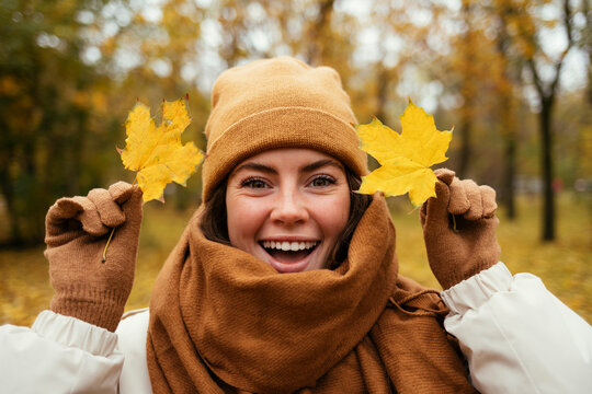 Cheerful young woman with autumn leafs in public park