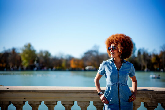 Smiling woman with hands in pockets looking away while standing against Estanque Grande Del Retiro pond, Spain