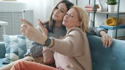 Joyful family mother and teen daughter are taking selfie posing for smartphone webcam sitting on couch at home. People and photjgraphy concept. - Powered by Adobe