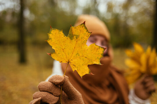 Young woman showing autumn leaf in public park