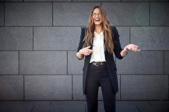 Happy businesswoman laughing while standing against brick wall