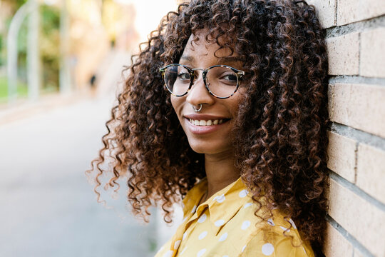 Young woman wearing eyeglasses smiling while leaning on wall