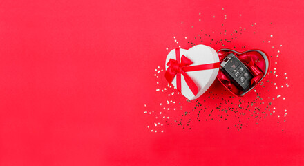 car keys in a white gift or present box with a red ribbon on red background decorated with confetti. Top view, Valentine's Day, women's day, car, holiday present concept, banner 