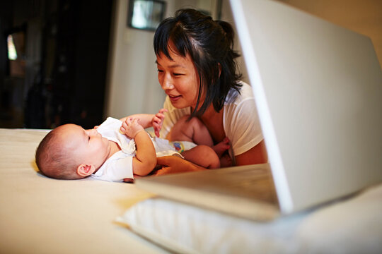 Mother and baby son lying on bed with laptop