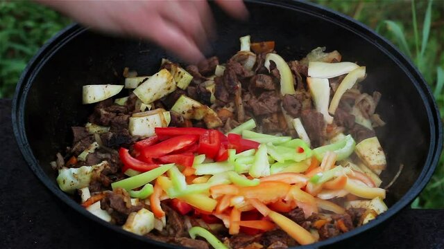 Meat with onions and zucchini stew in a large cauldron. In the dish add multicolored peppers, yellow, red, green. cooking traditional Asian food - lagman