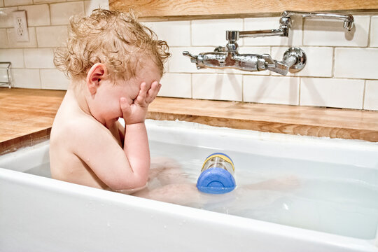 Male toddler playing peek a boo in bath