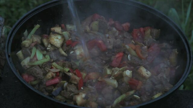 put eggplants in a big pot with meat, onions, carrots, zucchini. all ingredients are mixed with a wooden spatula. cooking on open fire