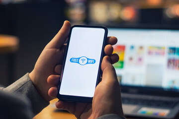 Man freelancer holds a smartphone with free internet in his hands on the background of a laptop.