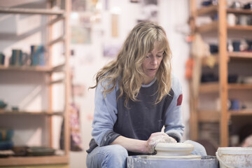 Female potter forming clay on pottery wheel in workshop