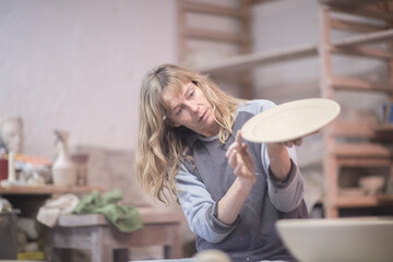 Female potter checking edge of plate in workshop