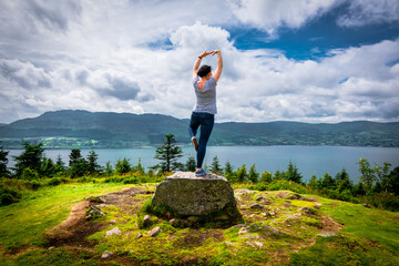 A woman standing on a rock, high on a hill, practicing yoga and enjoying views of the Atlantic...