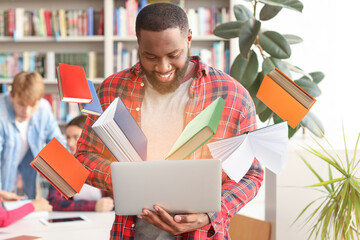 African-American student with laptop reading book online in library
