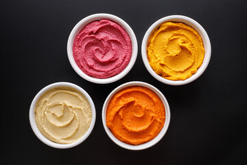 A set of hummus made of various vegetables in ceramic bowls on a black background, top view