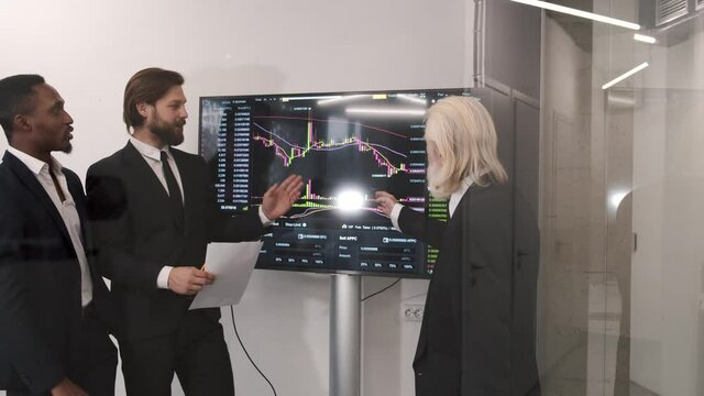 Trading stocks online. Businessmen working in office together, pointing at screen, discussion and checking global currency index on fund exchange