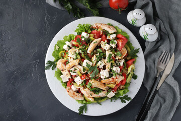Salad with bulgur, baked chicken, bell pepper, basil and feta on white plate on dark background, Closeup. Top view