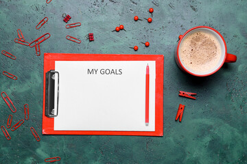Cup of coffee and clipboard with word GOAL on color background