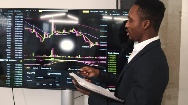 Trading stocks online. Businessman working in office standing at screen, discussing and checking global currency index on fund exchange.