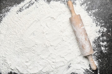 Wooden rolling pin and flour on dark background