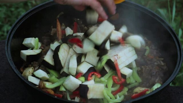 put eggplants in a big pot with meat, onions, carrots, zucchini. all ingredients are mixed with a wooden spatula. cooking on open fire