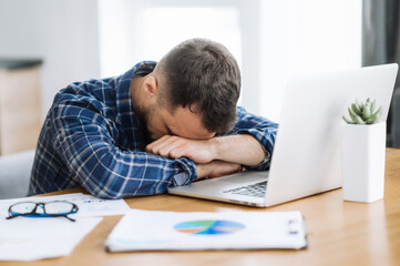 Tired freelancer man is fall asleep at the workplace. Exhausted busy guy working overtime, sits at the desk at home, need a rest, overwork concept. Work from home