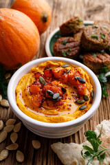Pumpkin hummus with the addition of roasted pumpkin and olive oil, sprinkled with pumpkin seeds in ceramic bowl on a rustic wooden table