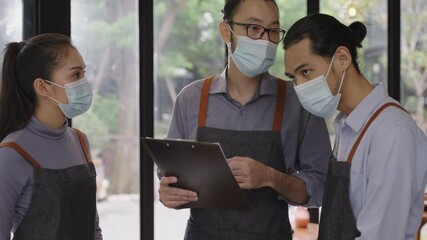 Asian male restaurant manager wearing face mask, explaining and assigning jobs to his colleagues, preparing for reopen after lockdown due to coronavirus pandemic with new normal business concept.