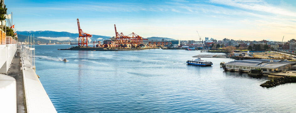 Vancouver Harbour panorama early mornings, on a sunny day. Waterfront city skyline with industry. A seabus ferry is leaving the waterfront station. Industrial cranes with cargo containers and tanker.