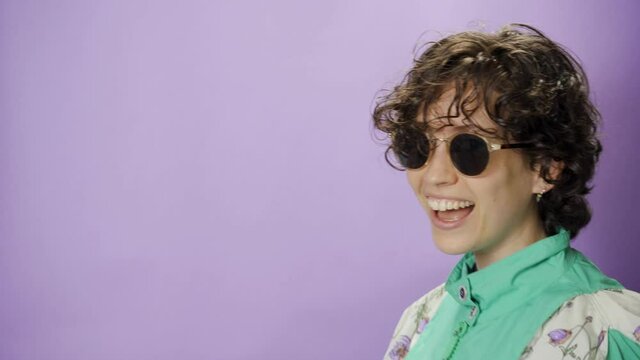 Funny happy woman with big smile crosses the frame while dancing with purple BG. Crazy dance moves eighties style with retro clothes and haircut. Moving from side to side walking backwards and enjoys