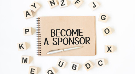 Text BECOME A SPONSOR on the craft colored notepad with block wood cubes on the white background
