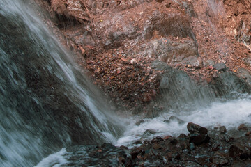 Pequeña cascada con fondo rocoso y rojizo 