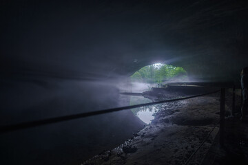 exit of an dark cave with underground river and some fog