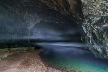 Fototapeta na wymiar underground river flows out of cave with fog