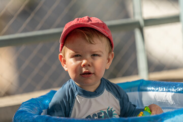 baby boy enjoying the swimming pool in the balcony on a hot summer day wearing a cap