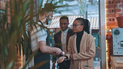Waiter in protective mask scanning body temperature of customers with infrared thermometer while standing at enter. Manager check temperature of people during covid-19 pandemic.Small business concept