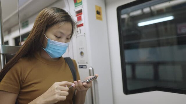 asian woman wearing protective face mask using smartphone on the public train