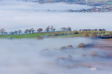 Trees emerging above banks of fog over farmland in a beautiful rural valley