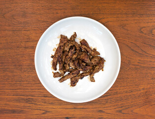 Fried marinated pork on white round ceramic plate. On the wooden background.