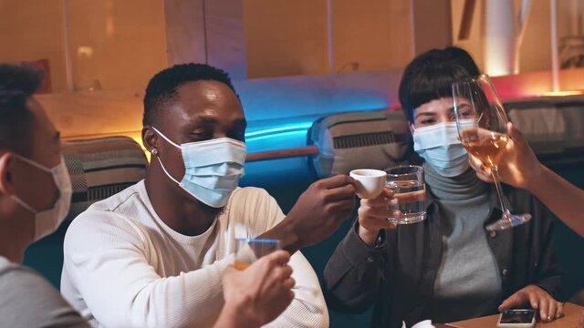 Diverse happy friends clinking glasses and cups with different beverages while celebrating something in restaurant. Multi ethnic friends toasting while enjoying dinner together in trendy cafe