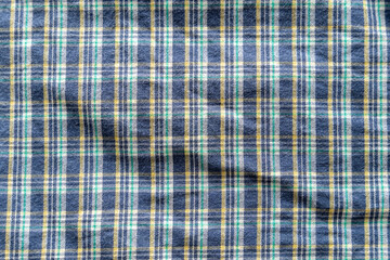 Plaid textile pattern of a blue green yellow garment. Fabric structure closeup of a vintage fashion clothing piece with wrinkles.