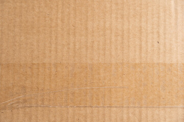 Brown cardboard texture with a transparent adhesive tape strip and some wrinkles. Carton structure of a packaging box used for shipping and delivery.