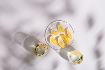 Life style photo with bright glass cups with fresh water and plate with citrus of lemon on white background. Summer minimal flat lay with hard shadows.