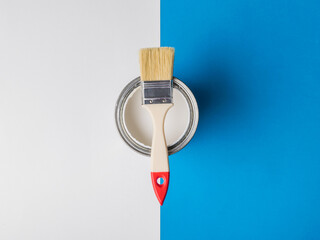 Brush on an open can of white paint on the border of two colors.