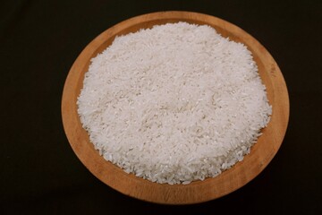 Rice in wooden plate, black background. Indonesia is the world's rice granary, healthy food and diet concept.