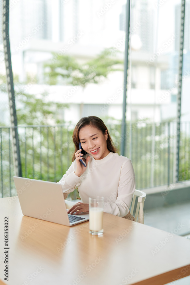 Poster single happy female business owner with smile on phone and working on laptop computer at desk with b