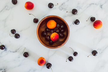 simple food ingredients, fresh apricots and cherries on marble background with wooden bowl