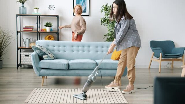 Mature mother and teenage daughter are doing housework cleaning house vacuuming floor and talking together. Household and family lifestyle concept.