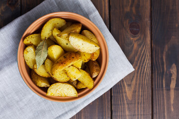 Slices of baked potatoes with herbs in a plate on a kitchen towel and a wooden table. Horizontal orientation, no people, copy space, close-up