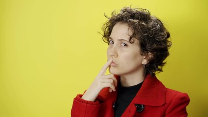 Professional looking young businesswoman thinking and wondering posture and pose. Female with red coat standing and contemplating with yellow background. Looks at camera.Trying to make sense of things