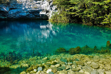 The amazing Blue Lake in Abkhazia is surrounded by sheer cliffs. Stones at the bottom and algae are visible through the clear turquoise water. Reflection on a shiny surface. Georgia.